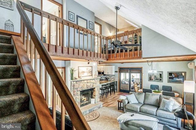 living room featuring a towering ceiling, a fireplace, hardwood / wood-style flooring, ceiling fan, and a textured ceiling