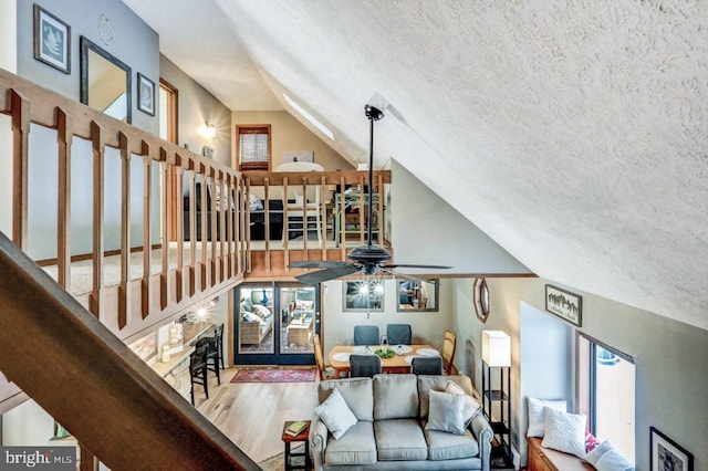 living room with hardwood / wood-style flooring, vaulted ceiling, ceiling fan, and a textured ceiling