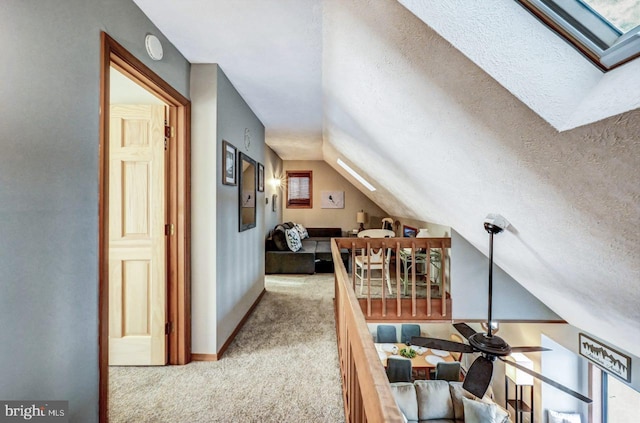 corridor with light colored carpet, vaulted ceiling with skylight, and a textured ceiling