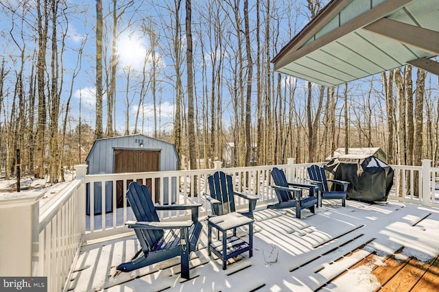 snow covered deck with area for grilling and a storage shed