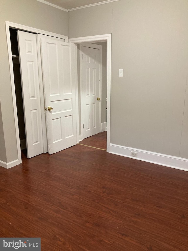 unfurnished bedroom featuring crown molding, dark wood-type flooring, and a closet