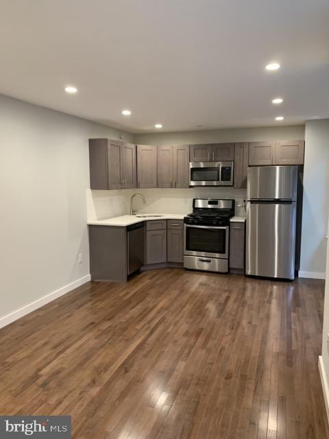 kitchen with appliances with stainless steel finishes, a sink, dark wood finished floors, and baseboards