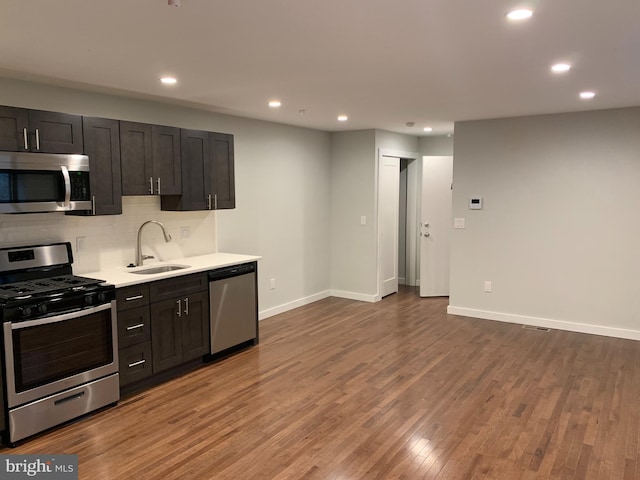 kitchen with baseboards, appliances with stainless steel finishes, wood finished floors, a sink, and backsplash