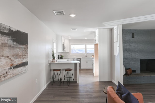 kitchen featuring appliances with stainless steel finishes, a breakfast bar area, white cabinets, kitchen peninsula, and dark wood-type flooring