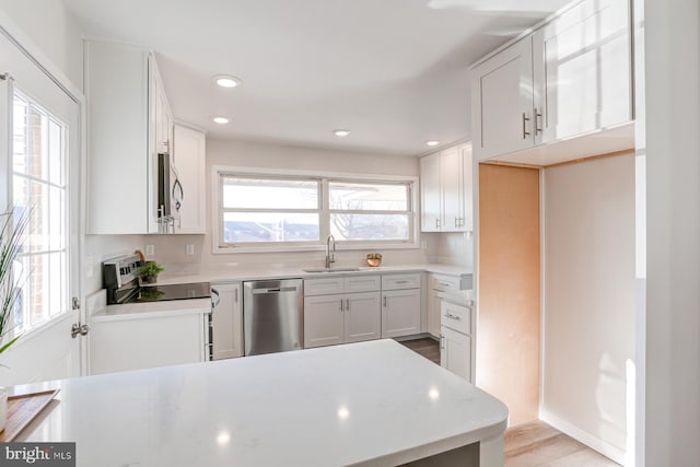 kitchen with stainless steel appliances, white cabinetry, sink, and light hardwood / wood-style flooring