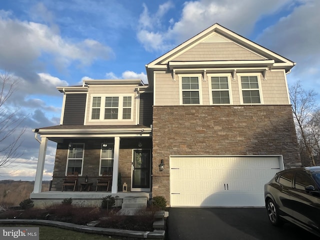 view of front of property featuring driveway, covered porch, a garage, and stone siding