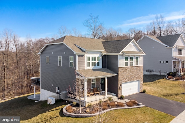 view of front of house with central AC unit, an attached garage, stone siding, driveway, and a front lawn