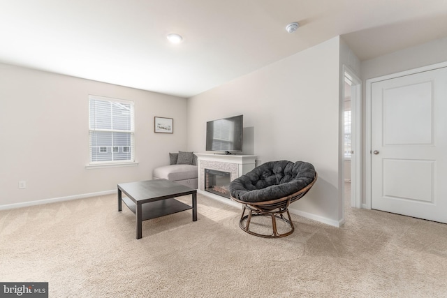 living area featuring baseboards, a glass covered fireplace, and light colored carpet