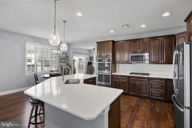 kitchen featuring dark wood-style floors, stainless steel appliances, light countertops, a kitchen island with sink, and a sink