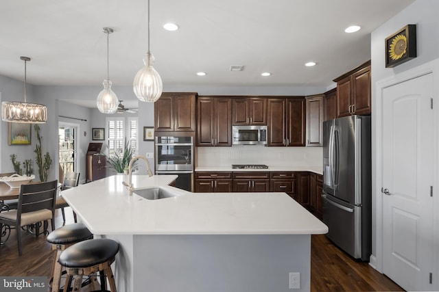 kitchen with dark wood-style floors, light countertops, appliances with stainless steel finishes, a sink, and a large island with sink