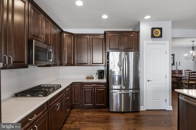 kitchen with a notable chandelier, recessed lighting, dark brown cabinets, appliances with stainless steel finishes, and dark wood finished floors