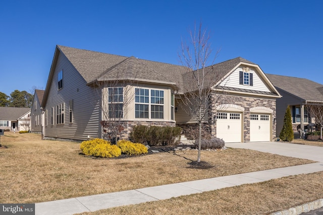 view of front facade featuring a standing seam roof, a garage, stone siding, driveway, and a front lawn