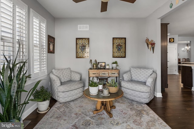 sitting room with ceiling fan with notable chandelier, wood finished floors, visible vents, and baseboards