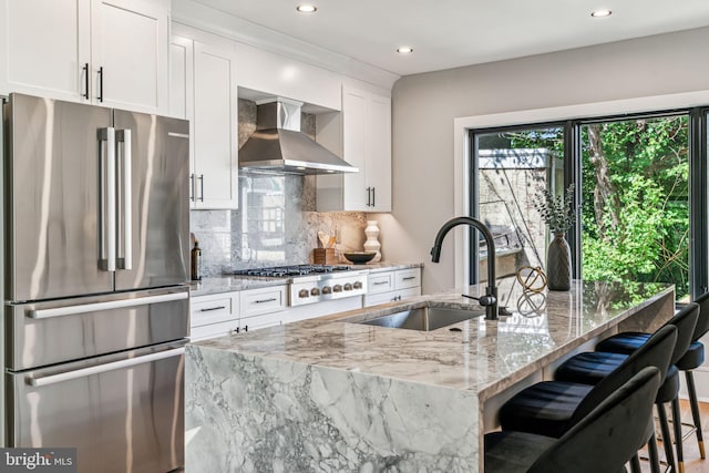 kitchen featuring wall chimney exhaust hood, sink, white cabinetry, light stone counters, and stainless steel appliances