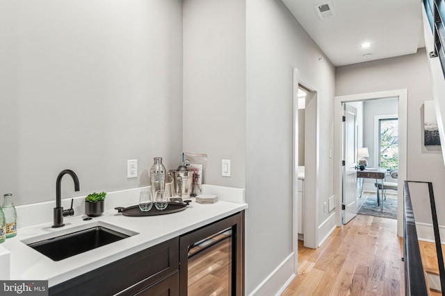 bar with wine cooler, sink, dark brown cabinets, and light wood-type flooring