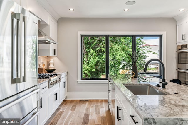 kitchen with sink, light hardwood / wood-style flooring, appliances with stainless steel finishes, white cabinetry, and light stone countertops