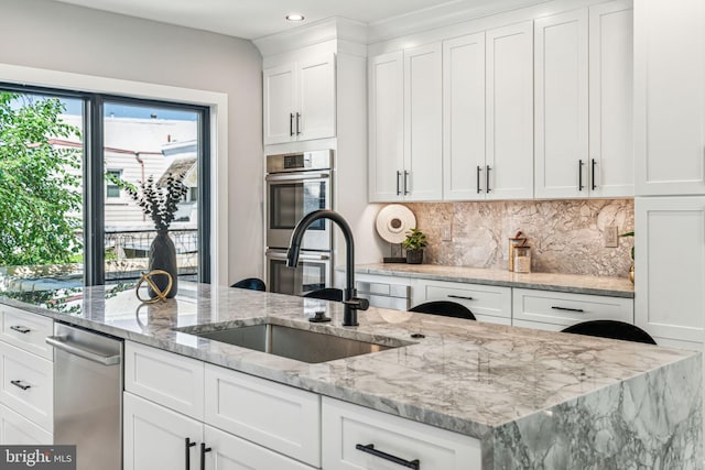 kitchen featuring double oven, white cabinetry, sink, backsplash, and light stone countertops