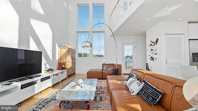 living area with a high ceiling, recessed lighting, and light wood-type flooring