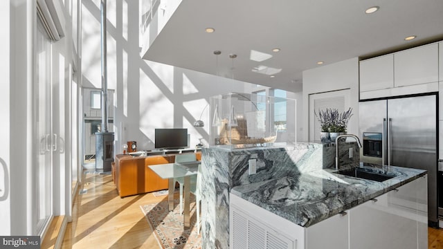 kitchen with a large island, stainless steel built in refrigerator, a sink, stone countertops, and recessed lighting