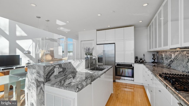 kitchen featuring backsplash, oven, light wood-style flooring, gas stovetop, and a sink