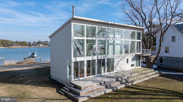 back of property with a yard, a water view, and a sunroom