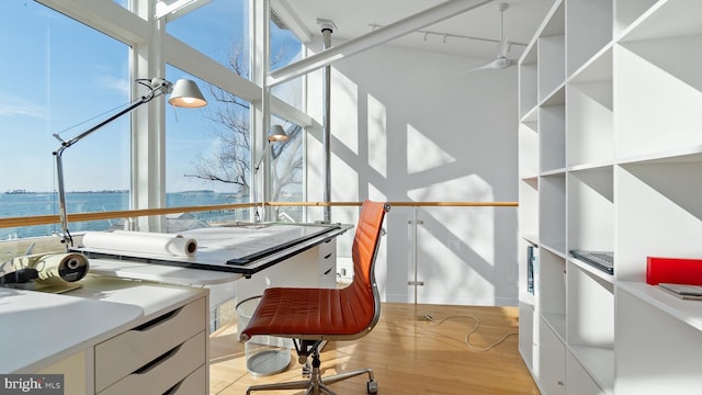 office area featuring a high ceiling, track lighting, light wood-style flooring, and a water view