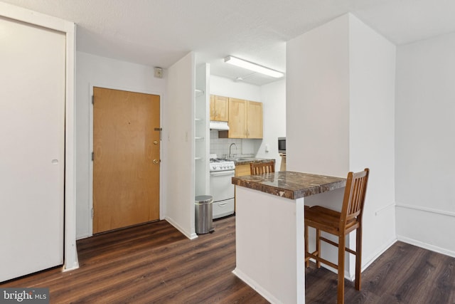 kitchen with white stove, light brown cabinetry, a breakfast bar area, kitchen peninsula, and dark wood-type flooring