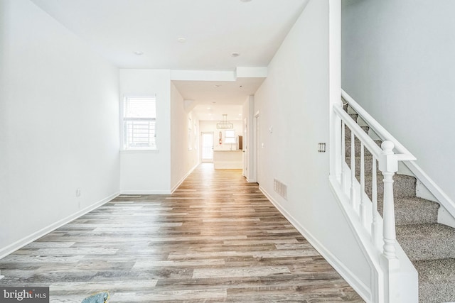 hall featuring baseboards, stairs, visible vents, and wood finished floors