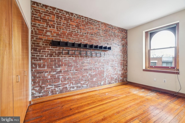 spare room featuring brick wall, baseboards, and wood-type flooring