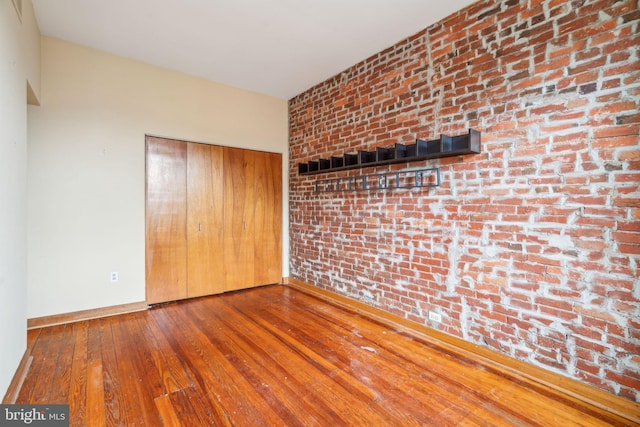 spare room featuring brick wall, baseboards, and hardwood / wood-style flooring