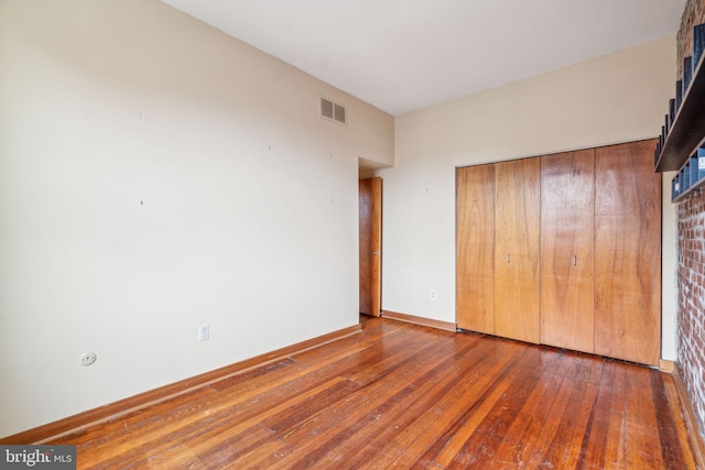 unfurnished bedroom with hardwood / wood-style floors, baseboards, visible vents, and a closet