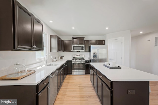 kitchen with appliances with stainless steel finishes, sink, a center island, dark brown cabinetry, and light wood-type flooring