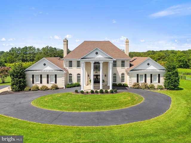 neoclassical home with a chimney, curved driveway, and a front yard