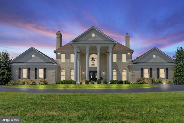 neoclassical / greek revival house with french doors, a chimney, a front yard, and brick siding