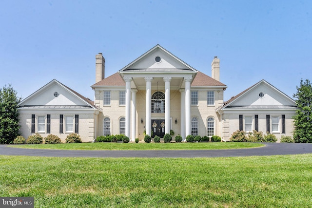 neoclassical home with brick siding, a chimney, a front lawn, and french doors