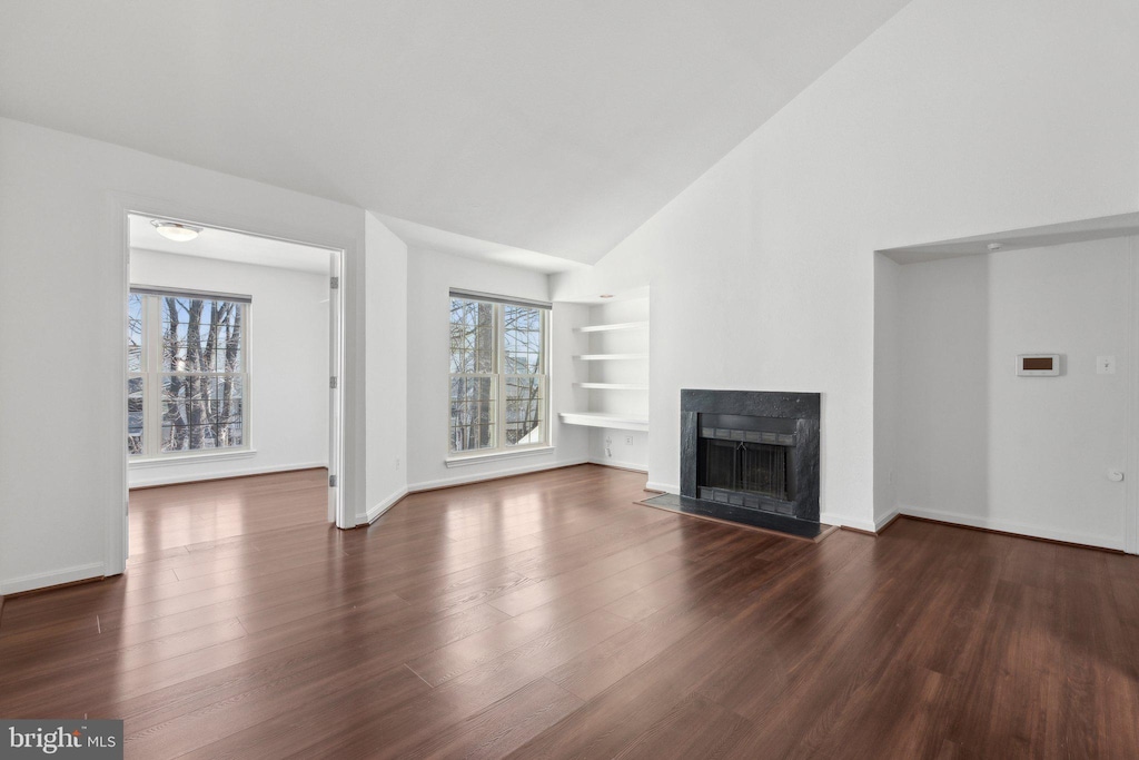 unfurnished living room featuring dark wood-type flooring, built in features, and high vaulted ceiling