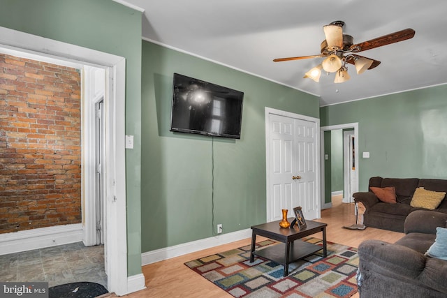 living room featuring wood-type flooring, brick wall, ornamental molding, and ceiling fan