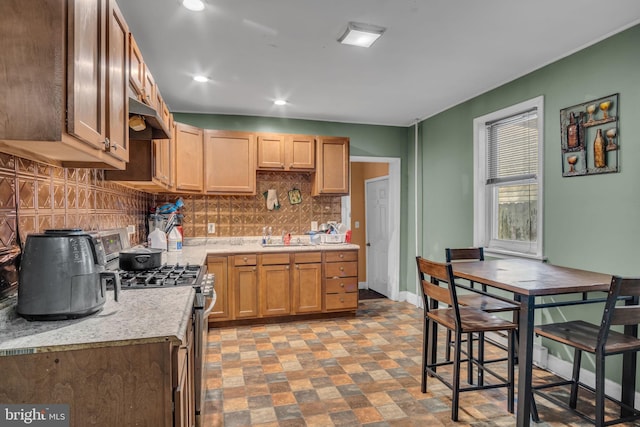 kitchen featuring tasteful backsplash, sink, stainless steel gas range, and light stone counters