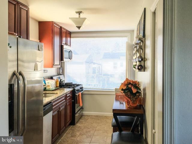 kitchen with reddish brown cabinets, light tile patterned floors, stainless steel appliances, stone countertops, and baseboards