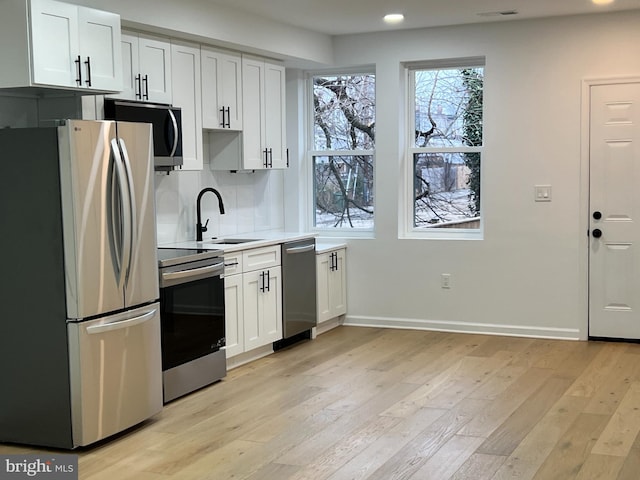kitchen featuring sink, white cabinetry, stainless steel appliances, decorative backsplash, and light wood-type flooring