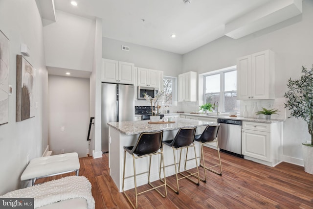 kitchen with appliances with stainless steel finishes, dark hardwood / wood-style floors, light stone countertops, white cabinets, and a kitchen island