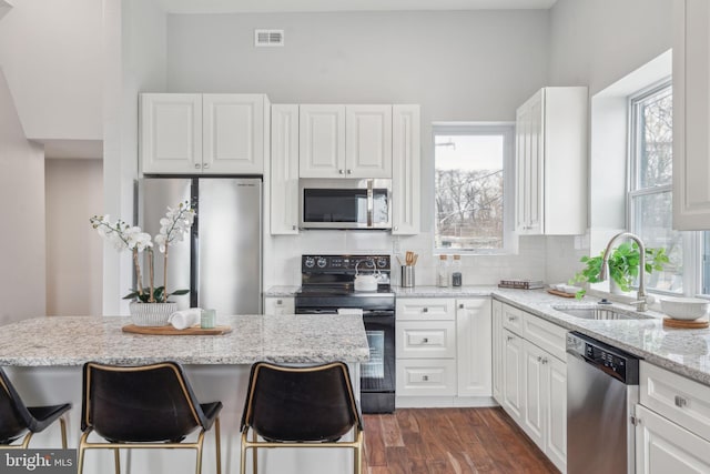 kitchen featuring appliances with stainless steel finishes, sink, white cabinets, backsplash, and light stone countertops