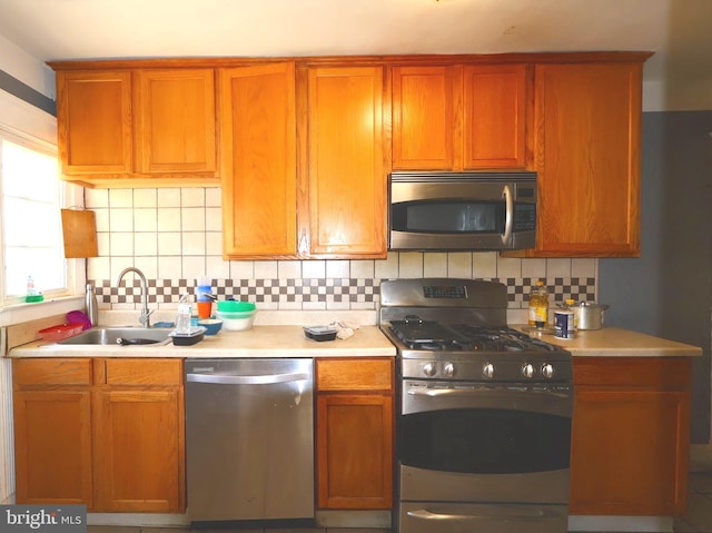 kitchen featuring tasteful backsplash, brown cabinetry, appliances with stainless steel finishes, light countertops, and a sink