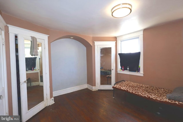 unfurnished bedroom featuring dark wood-style floors, baseboards, and arched walkways