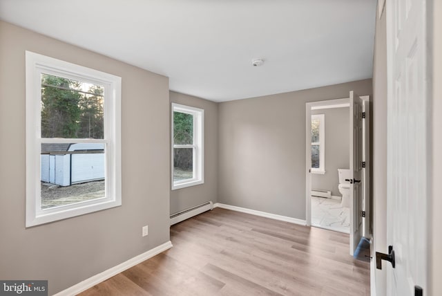 spare room with a baseboard radiator, baseboards, and light wood-style flooring