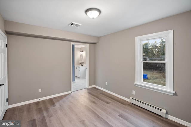 unfurnished bedroom featuring a baseboard radiator, visible vents, ensuite bathroom, light wood-style floors, and baseboards