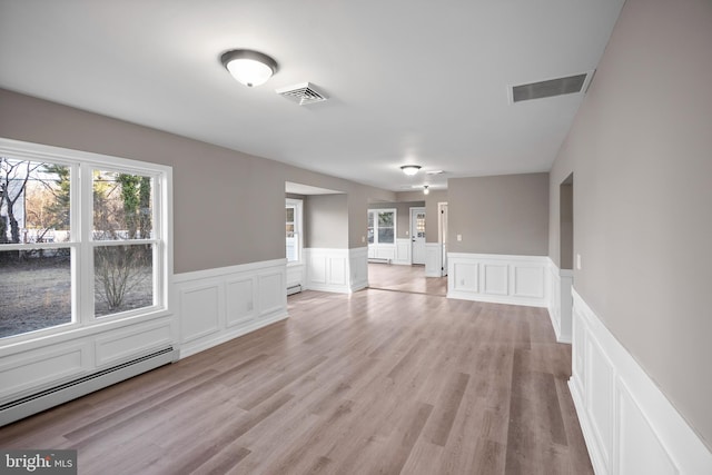 interior space featuring a baseboard heating unit, light wood-style flooring, baseboard heating, and visible vents