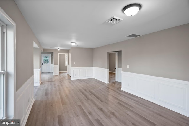 unfurnished room with light wood-style flooring, visible vents, and wainscoting