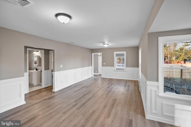 unfurnished room with wainscoting, light wood-type flooring, visible vents, and a healthy amount of sunlight