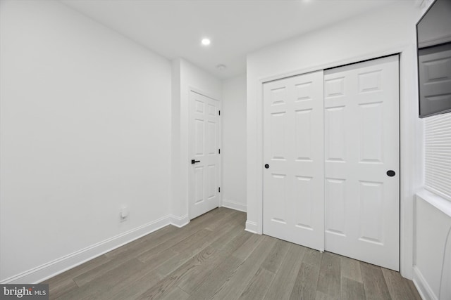 unfurnished bedroom with light wood finished floors, baseboards, a closet, and recessed lighting